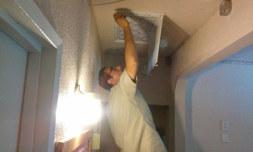 Person reaching up to ceiling vent in hallway with bright light.