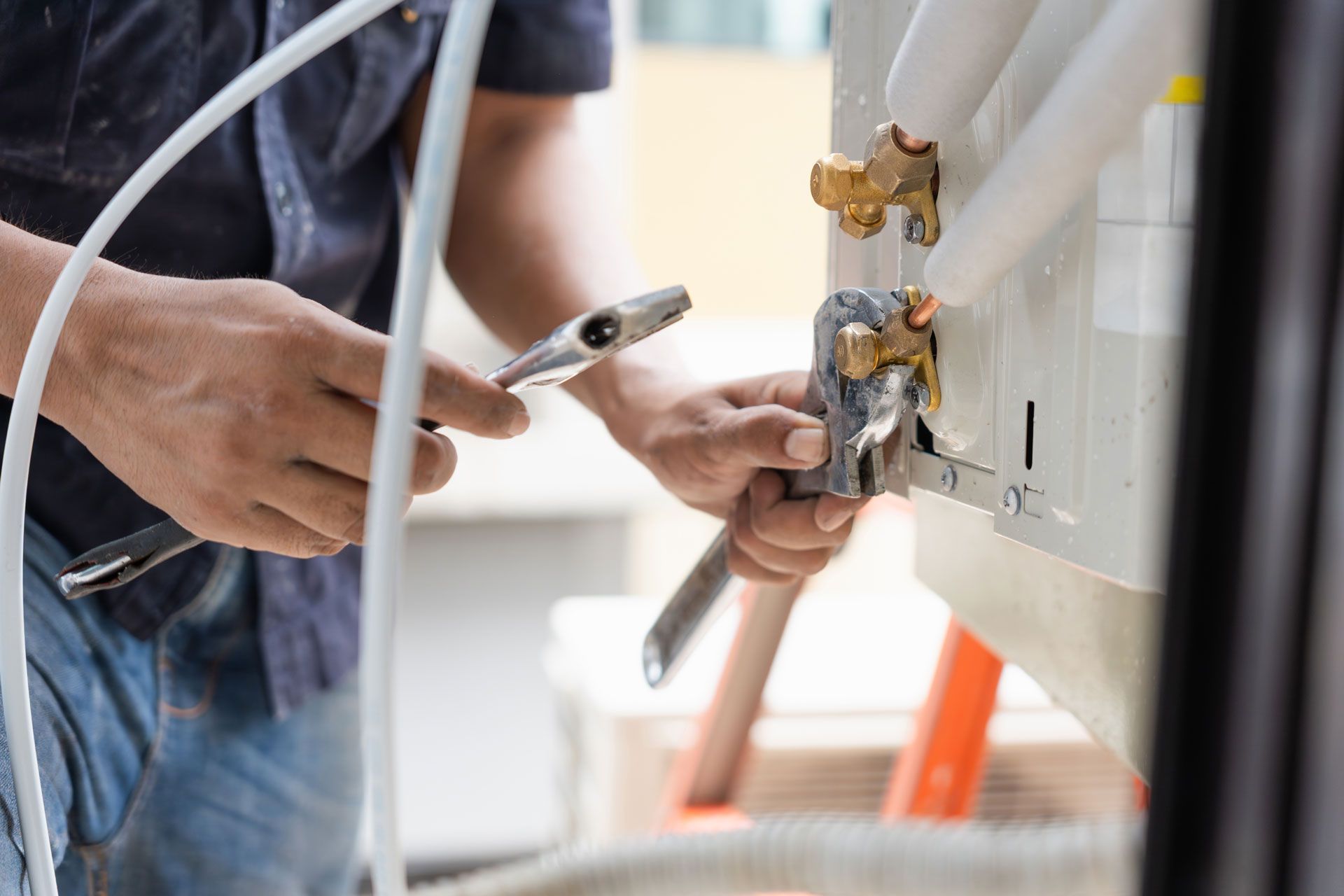 HVAC technician using tools to connect copper pipes to an air conditioning unit.