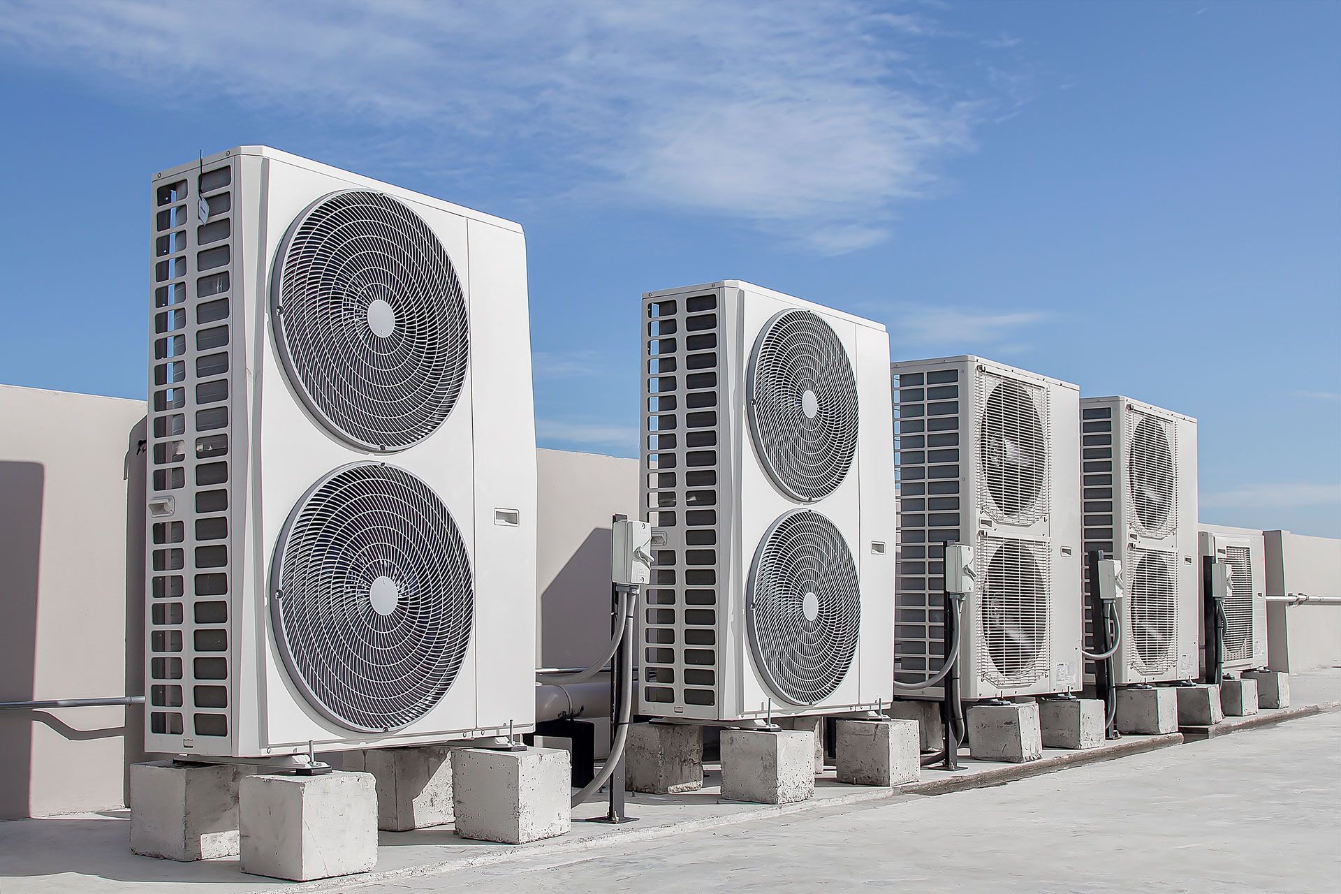 Air conditioning units lined up on a rooftop against a blue sky.