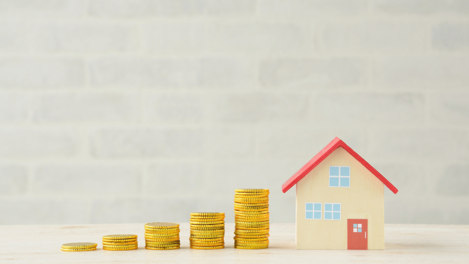 Stacks of gold coins rising to a small house, symbolizing financial growth in real estate.