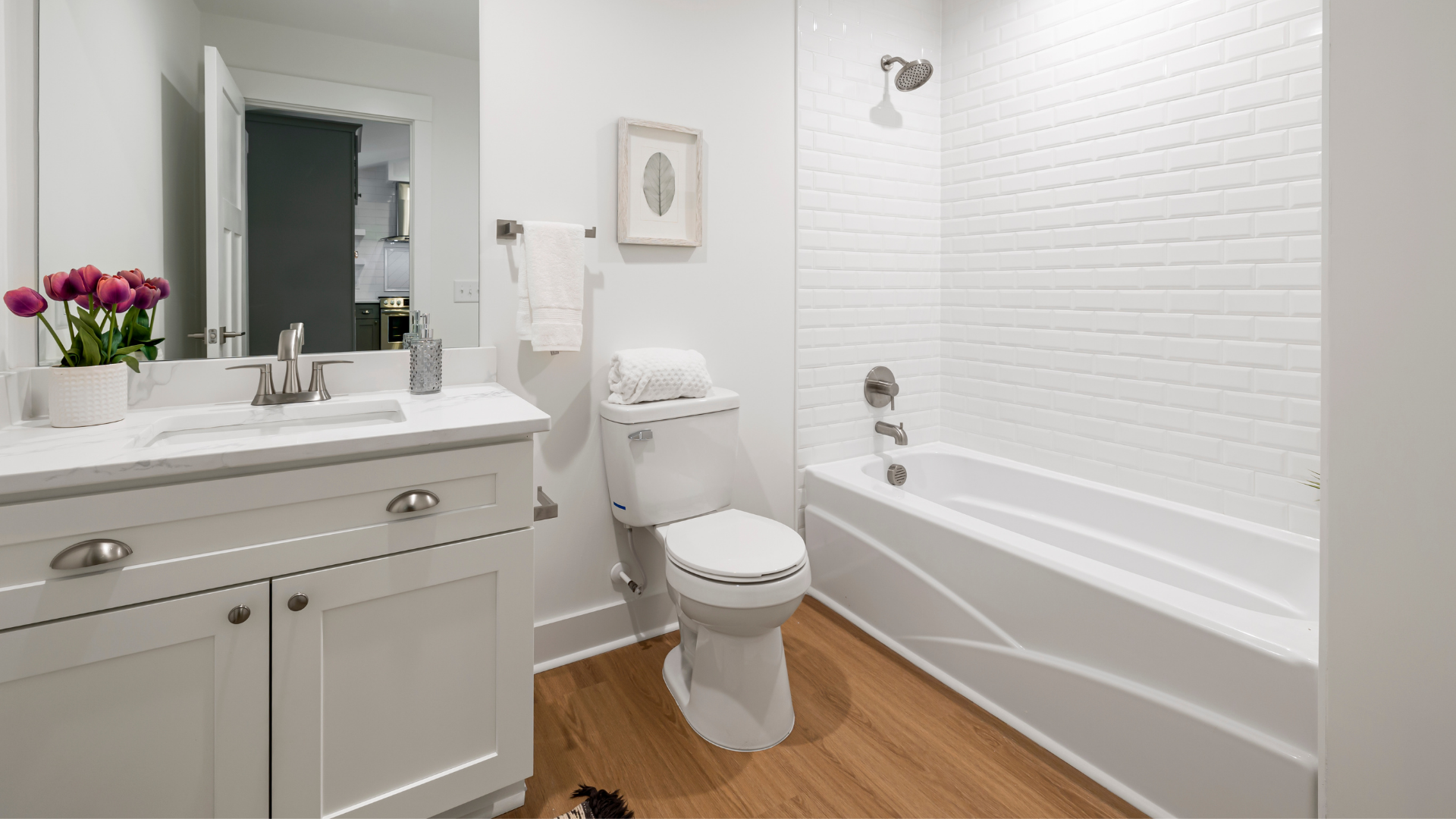Bright white bathroom with vanity, toilet, and bathtub on wood-look floor.