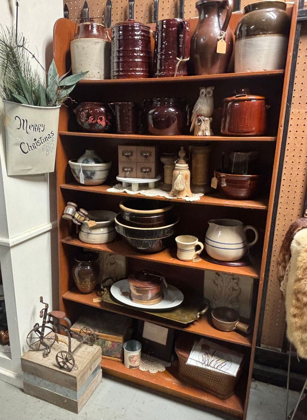 Shelves with rustic pottery, dishes, and a clock, arranged against a gray wall on a wooden table.