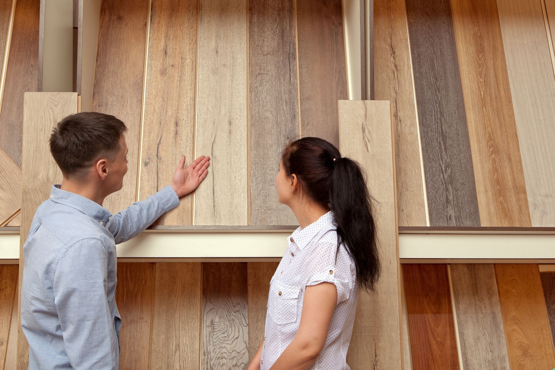Couple examining wood flooring plank samples displayed on a showroom wall.