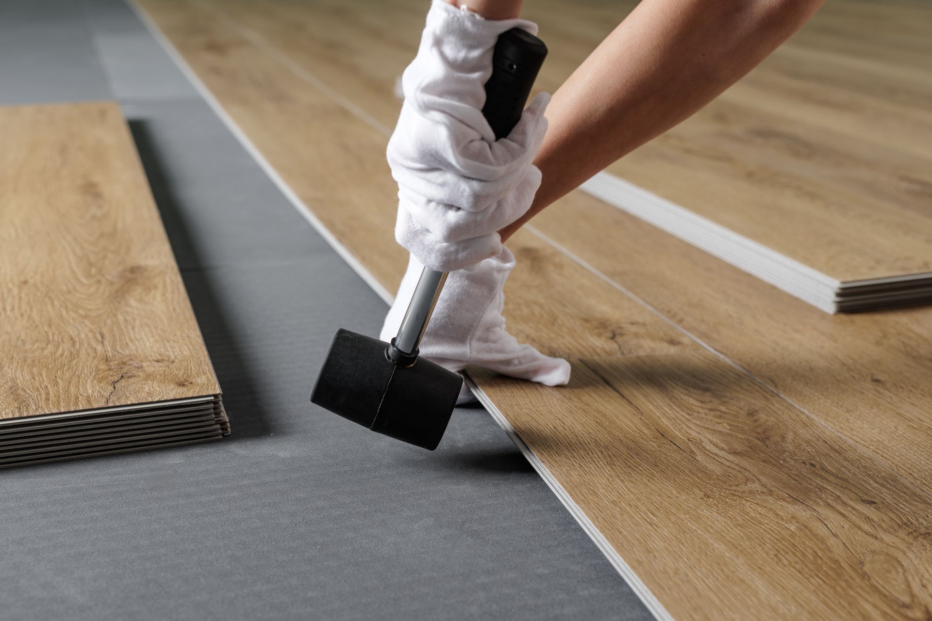 Installer in white gloves tapping vinyl plank flooring into place with a rubber mallet