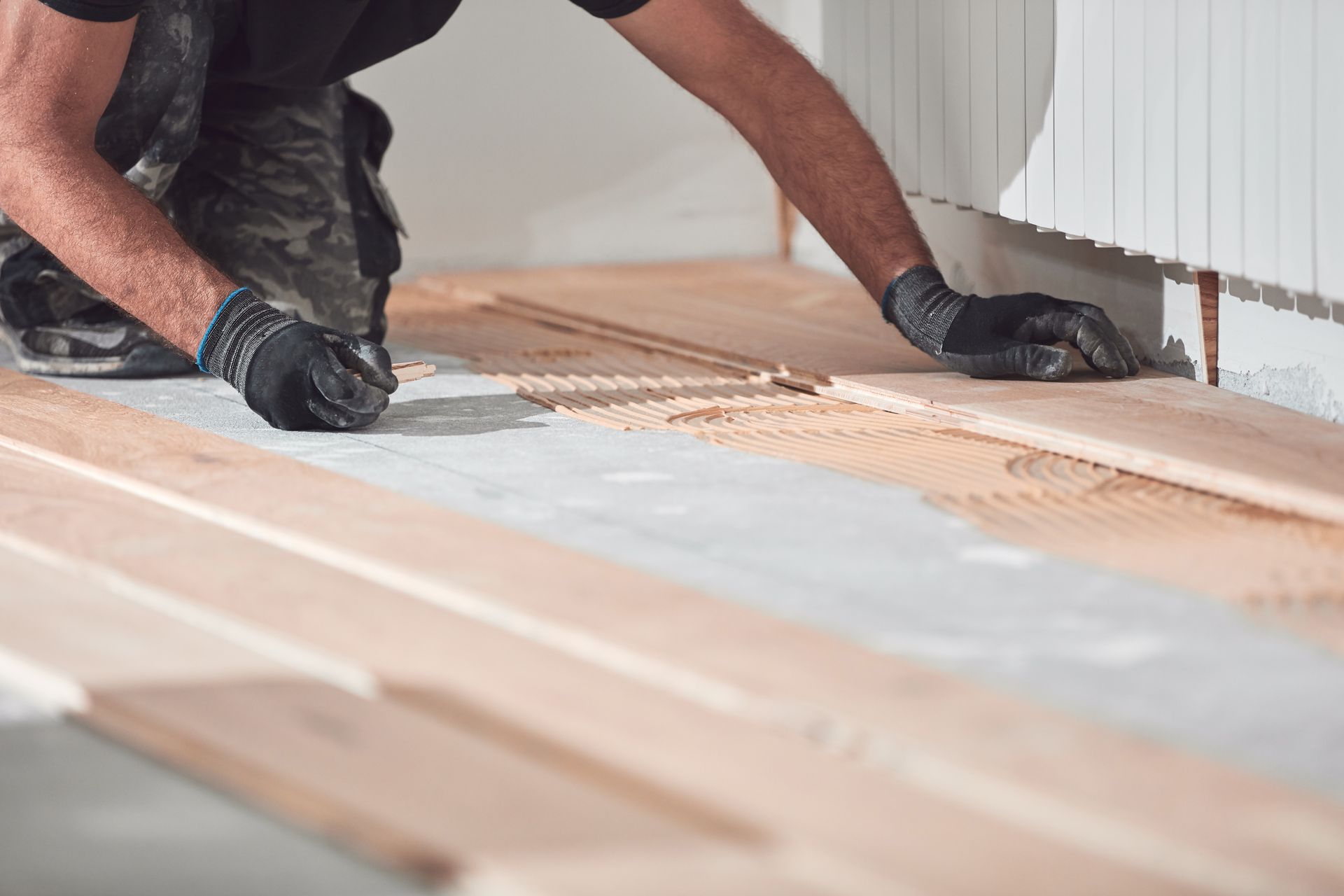 a person installing wooden flooring, spreading adhesive on the floor before placing wooden planks.