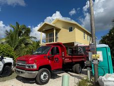 Red pickup truck parked beside a yellow house and blue portable toilet under a cloudy sky