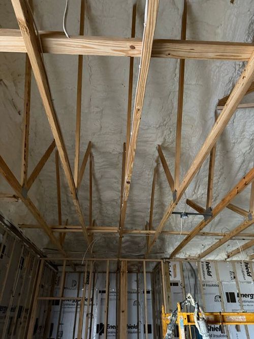 Exposed wooden roof trusses and metal framing inside a construction site with scaffolding below