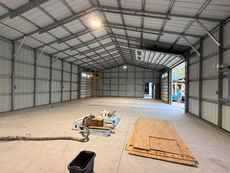 Empty metal warehouse interior with concrete floor, tools and plywood stacked near the center.