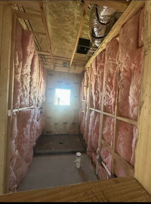Unfinished hallway with exposed pink insulation, wood framing, and a bright window at the end.