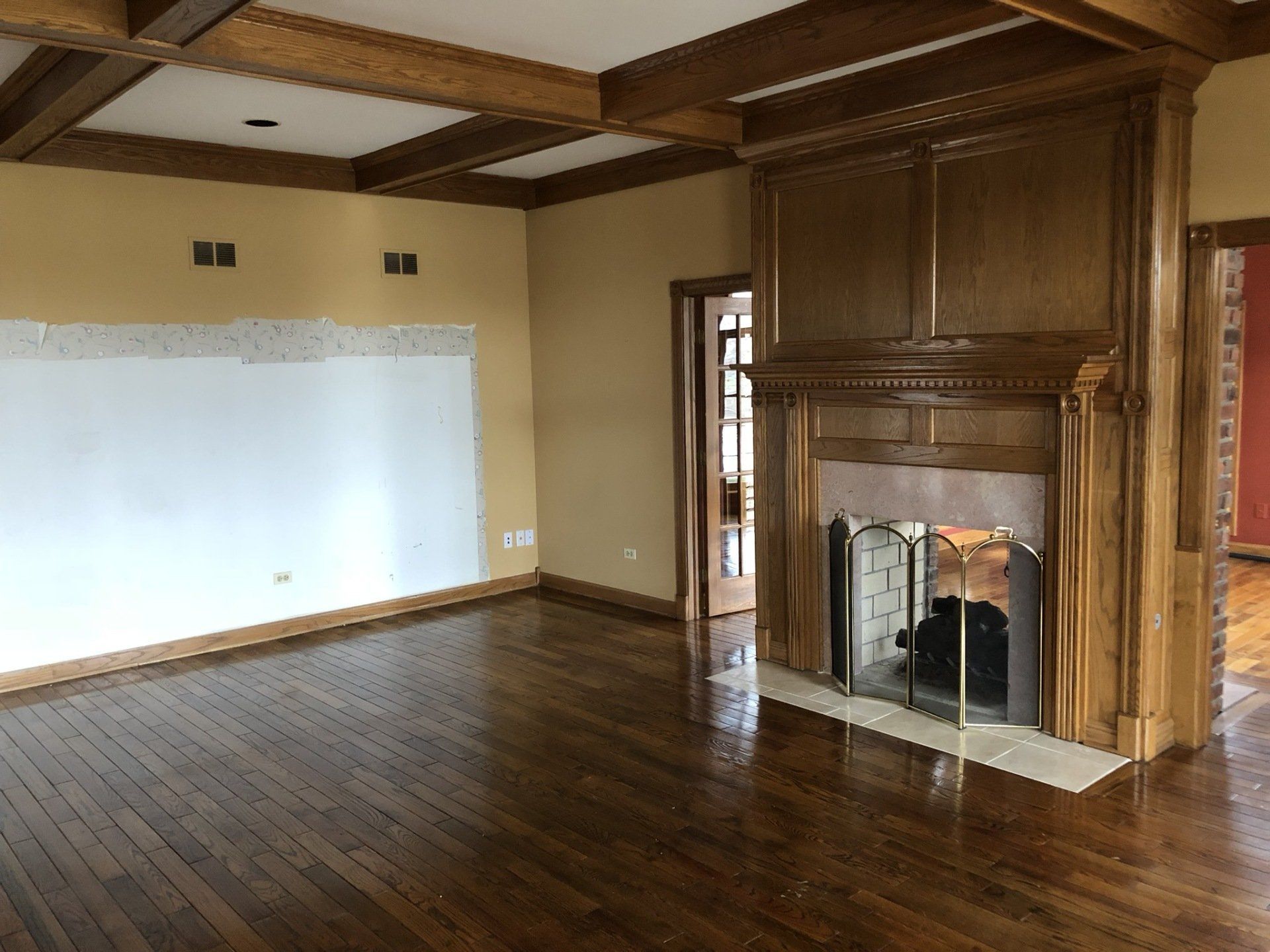 Empty room with dark wood floors, coffered ceiling, large fireplace, and whiteboard wall
