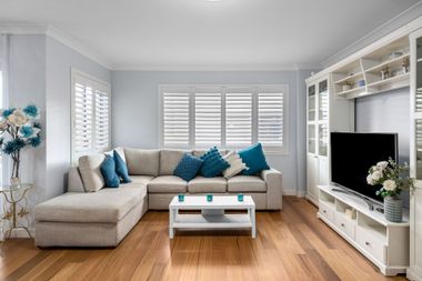 Bright living room with gray sectional sofa, blue cushions, white TV cabinet, and wooden floors