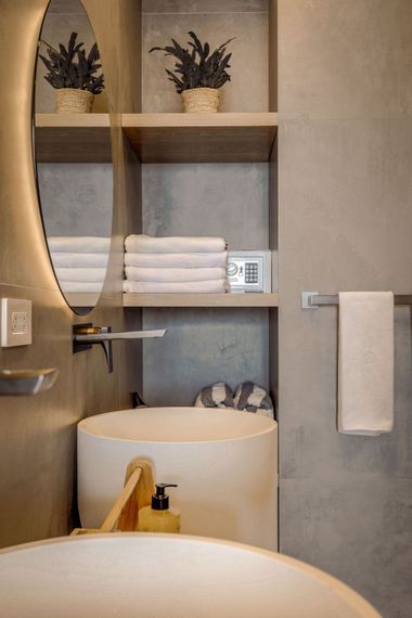 Modern bathroom vanity with round mirror, open shelf towels, plants, and a white vessel sink