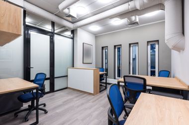 Modern office with blue chairs, wood desks, frosted glass walls, and white exposed ceiling pipes