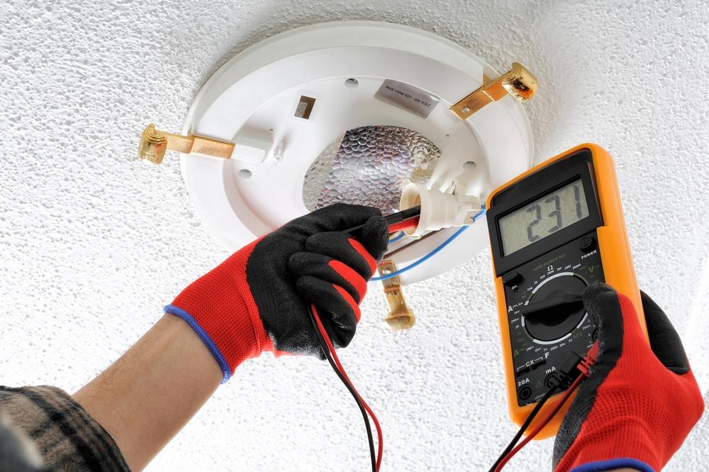 A Man is Using a Multimeter to Test a Ceiling Light — Atherton Electrical in Mareeba, QLD