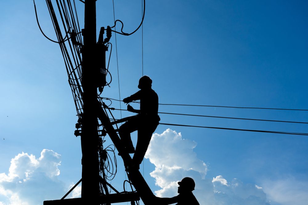 Silhouetted Utility Workers on a Power Pole Against a Blue Sky — Atherton Electrical in Mareeba, QLD