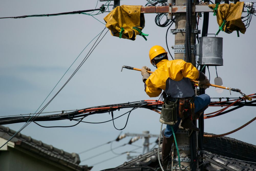 Electrician In Yellow Protective Gear Working On Power Lines Attached To A Utility Pole — Atherton Electrical in Cairns, QLD