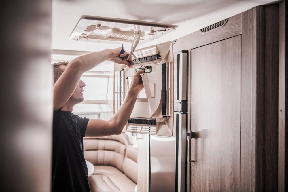 A Man is Working on a Refrigerator in a RV — Atherton Electrical in Atherton, QLD