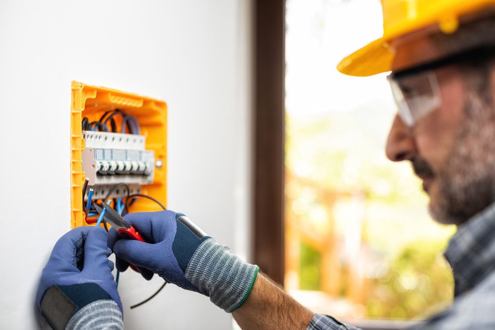 An Electrician is Working on an Electrical Box on a Wall — Atherton Electrical in Atherton, QLD