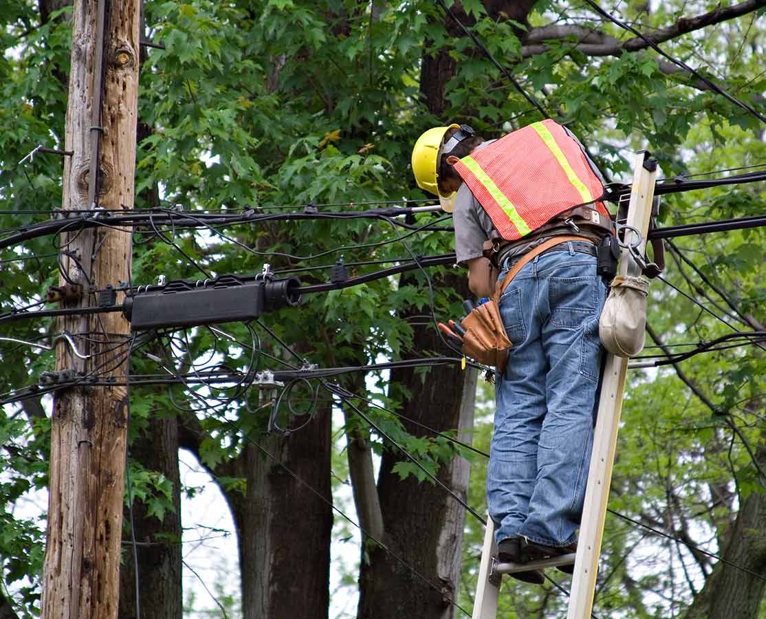 A Man is Standing on a Ladder Working on a Power Line — Atherton Electrical in Atherton, QLD