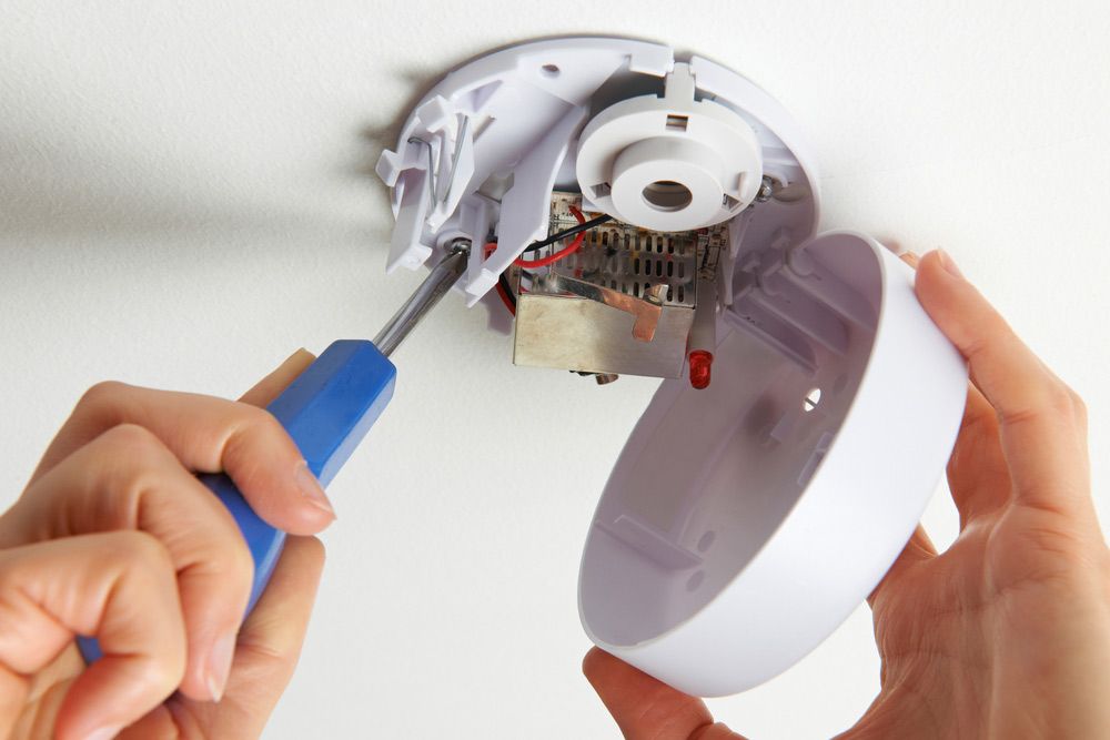 A Person is Fixing a Smoke Detector With a Screwdriver — Atherton Electrical in Atherton, QLD
