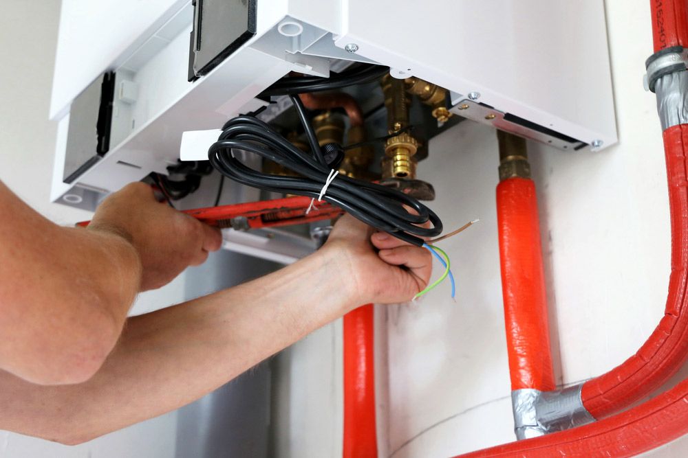 A Man is Fixing a Boiler With a Wrench — Atherton Electrical in Atherton, QLD