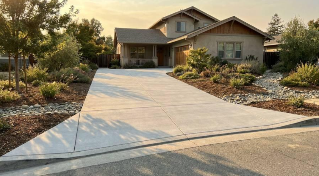 Suburban house with a long concrete driveway and landscaped front yard at sunset