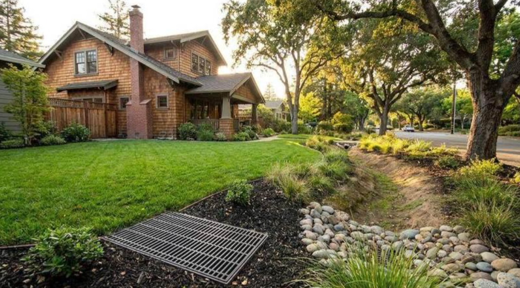 Brick house with a lush green lawn, trees, and a rocky drainage bed in the foreground