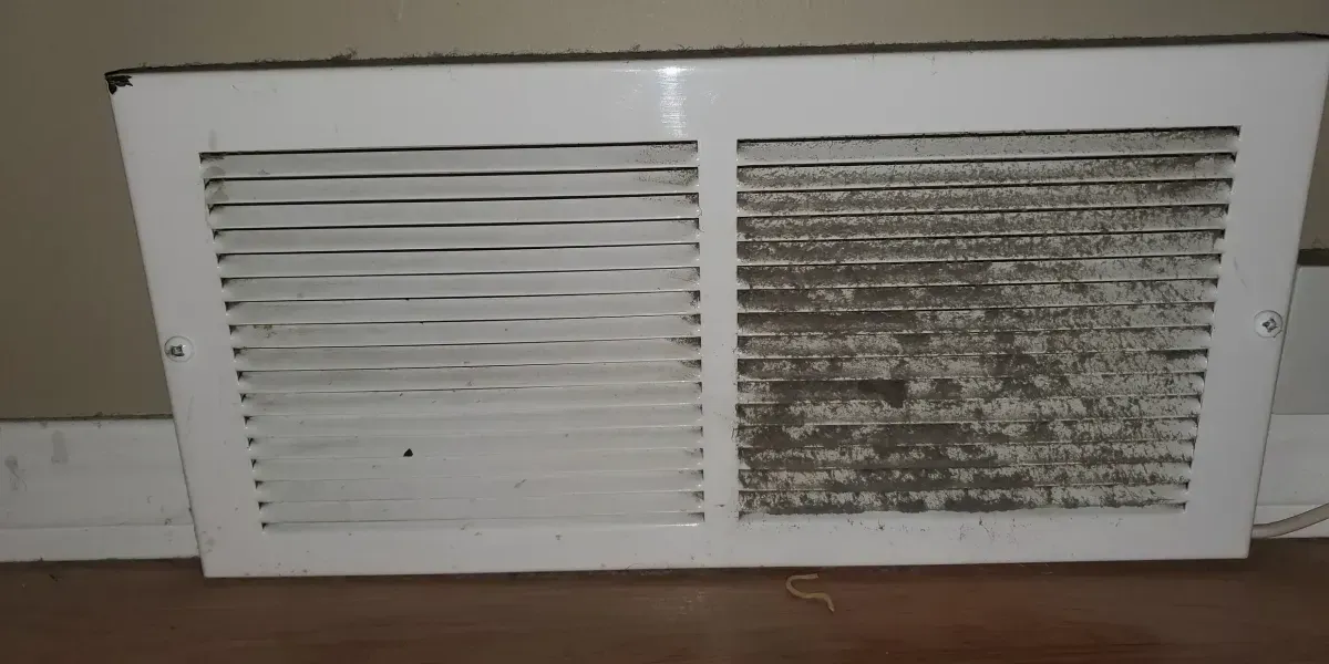 White wall vent cover with two louvered panels, one clean and one dirty with dark grime