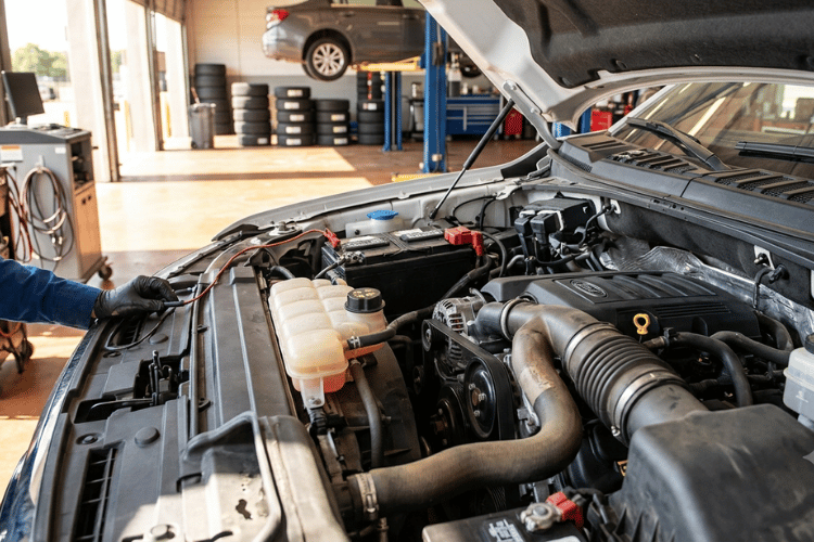 Close-up of a vehicle engine bay with the hood open inside a professional auto repair shop