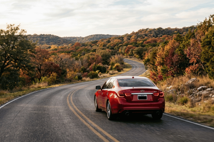 Red Infiniti sedan driving along a winding Central Texas road surrounded by fall foliage