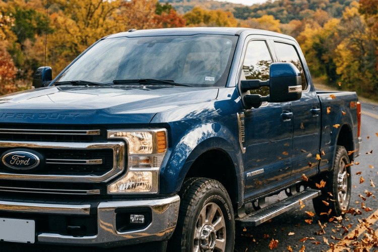 Blue Ford Super Duty diesel pickup driving on a fall road surrounded by colorful foliage
