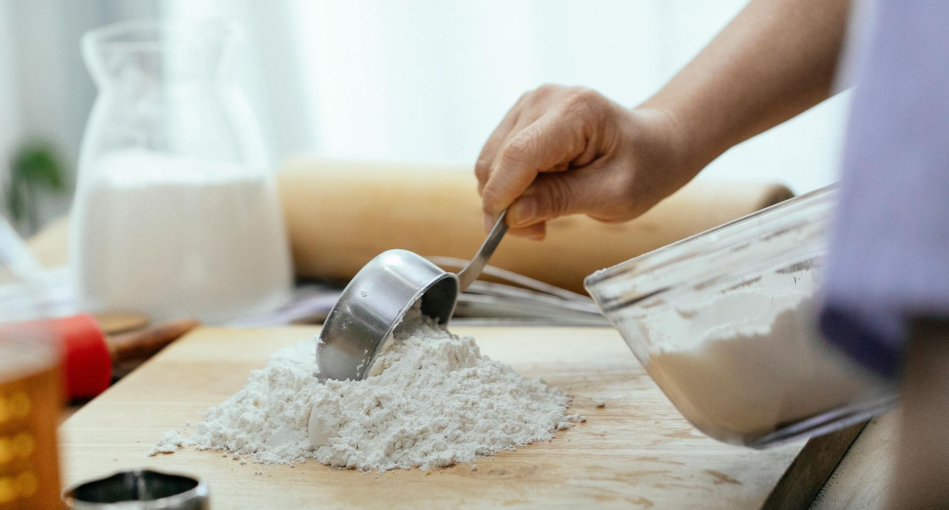 A person is pouring extra flour into a measuring cup on a cutting board.