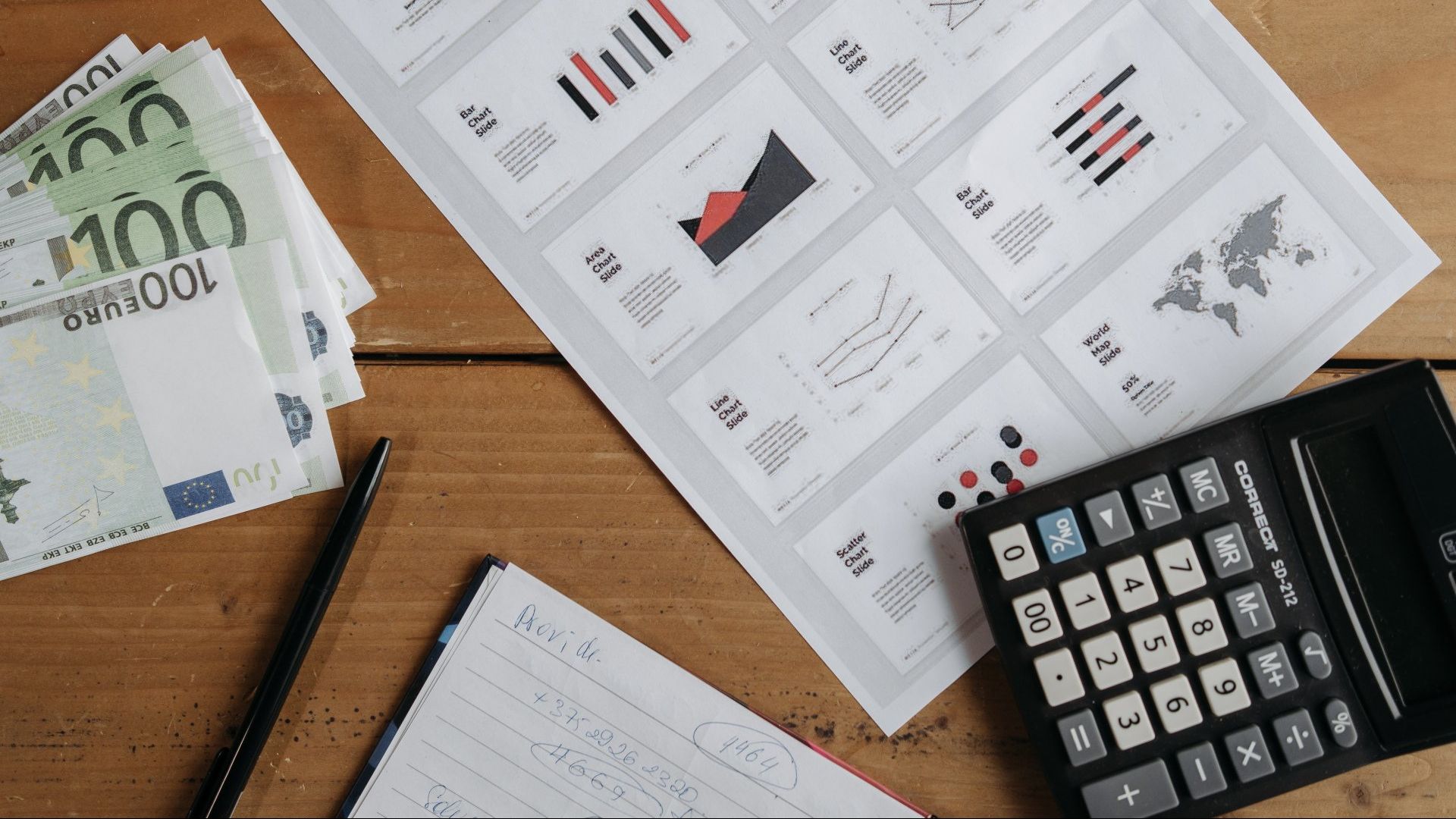 A calculator is sitting on a wooden table next to a stack of money.