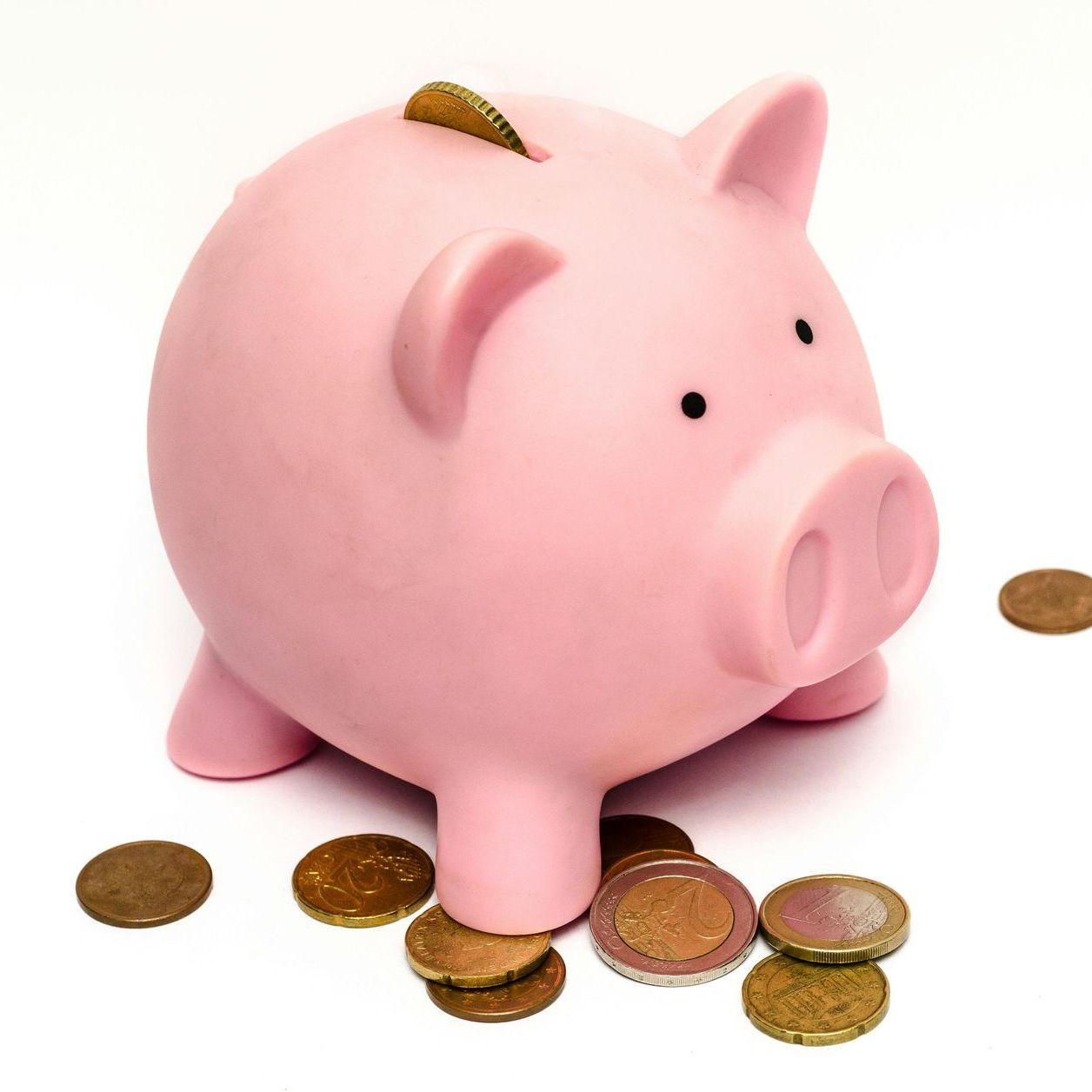 A pink piggy bank surrounded by coins on a white background