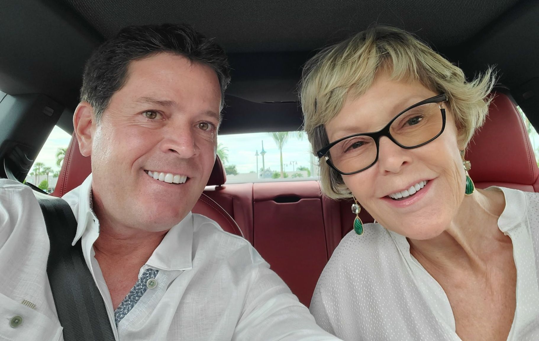 A man and a woman are sitting in a car and smiling for the camera.