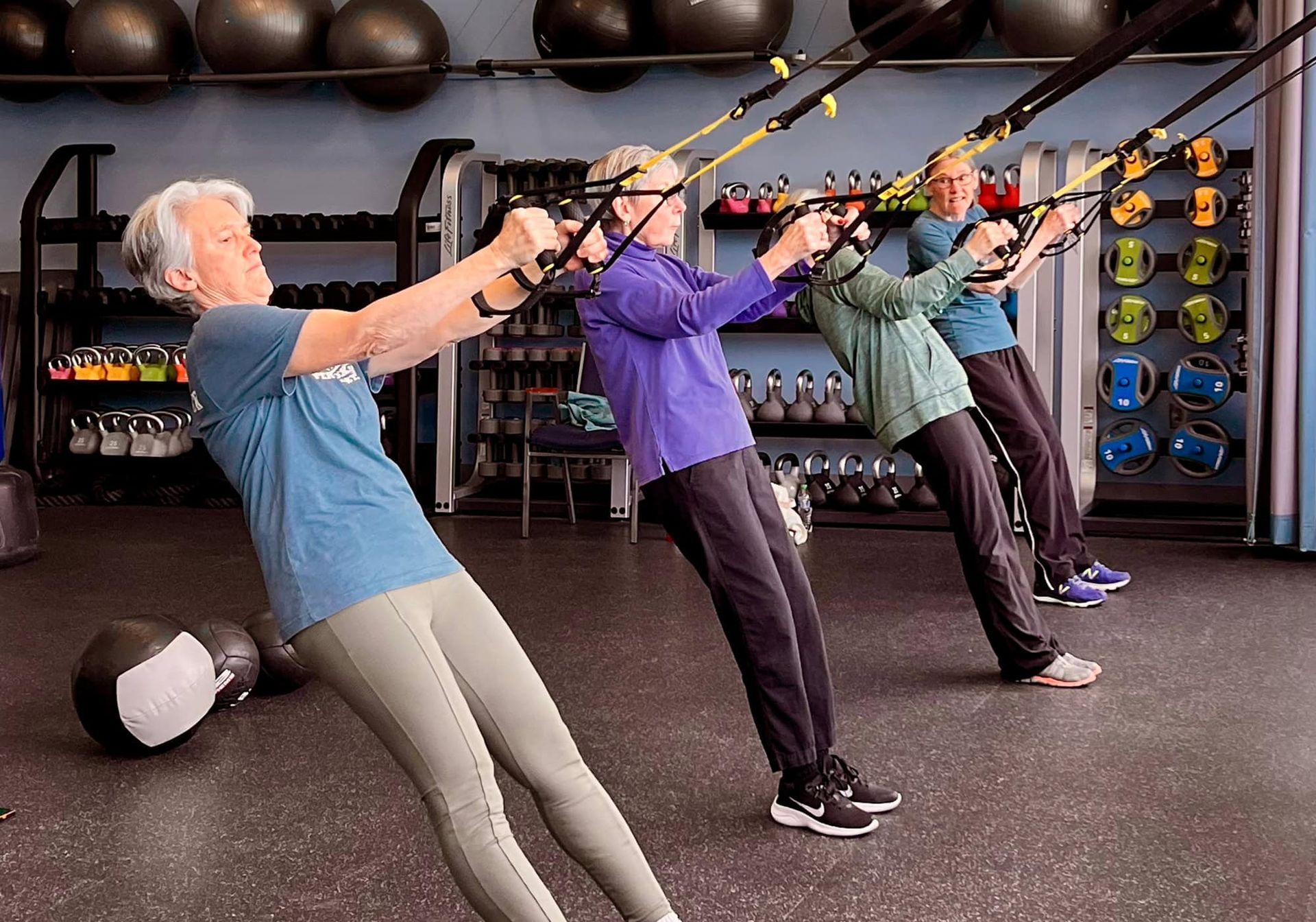 A group of older women are doing trx exercises in a gym.