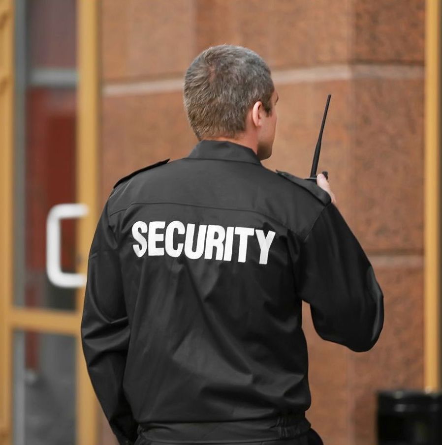 A man wearing a black security jacket talking on a walkie talkie