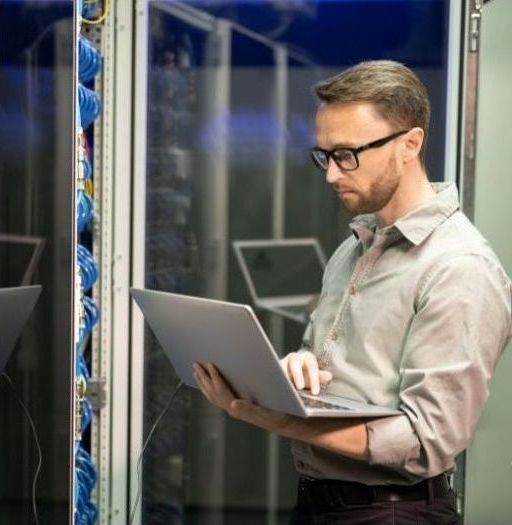 A man is using a laptop computer in a server room.
