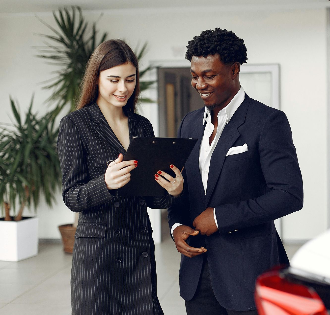 A man and a woman are looking at a clipboard in a car showroom.