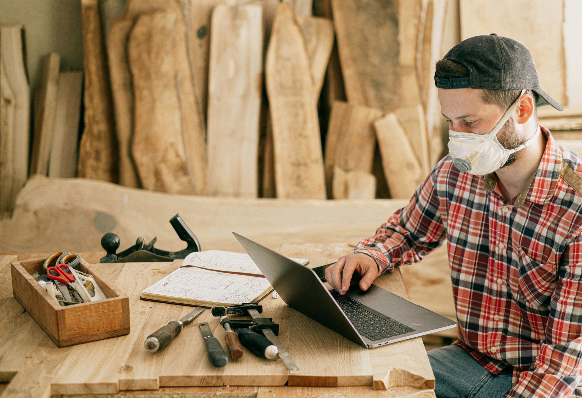 A man wearing a mask is sitting at a table using a laptop computer.