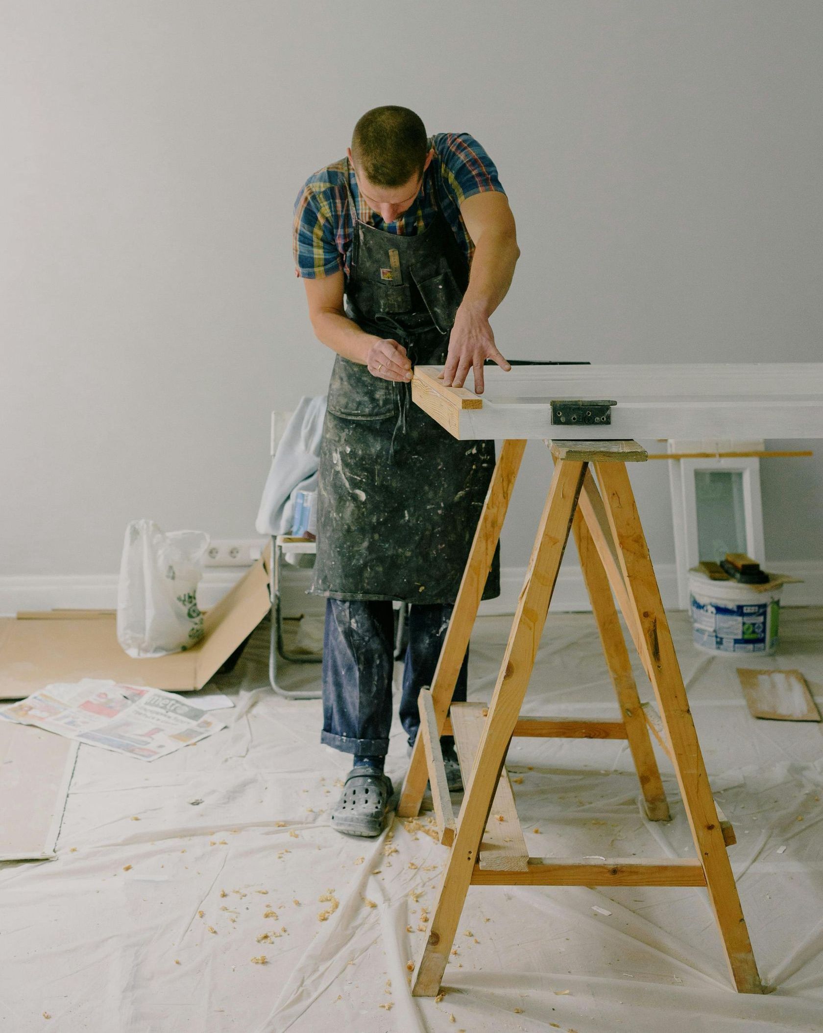 A man is standing on a wooden trestle painting a wall.