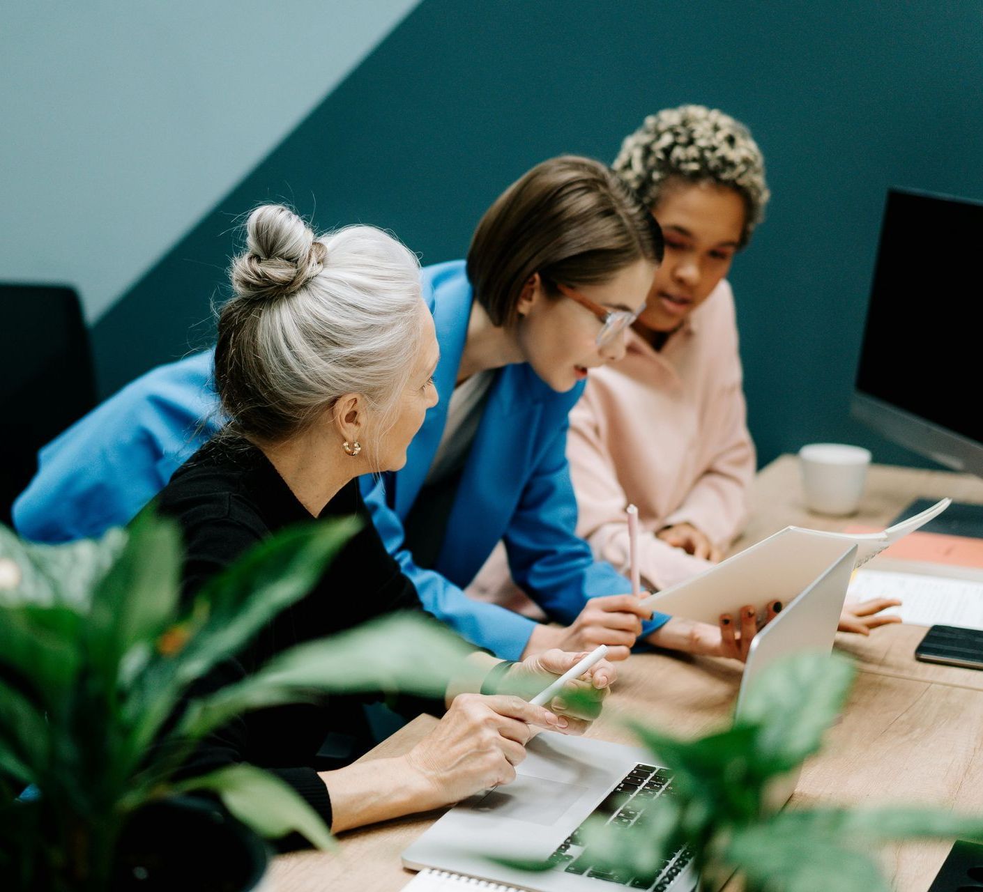 Three women are sitting at a table looking at a laptop