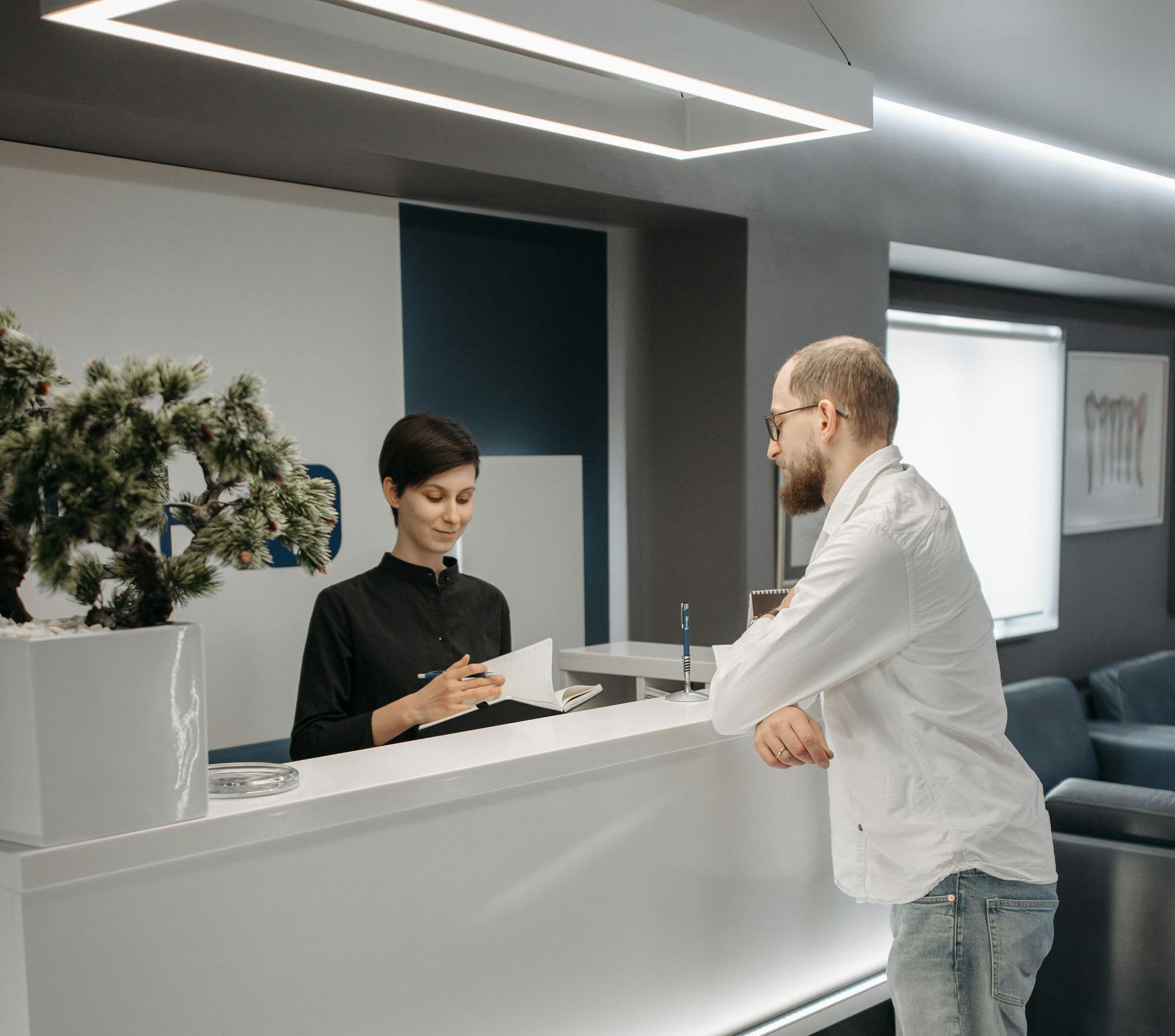A man is talking to a woman at a reception desk in a hospital.