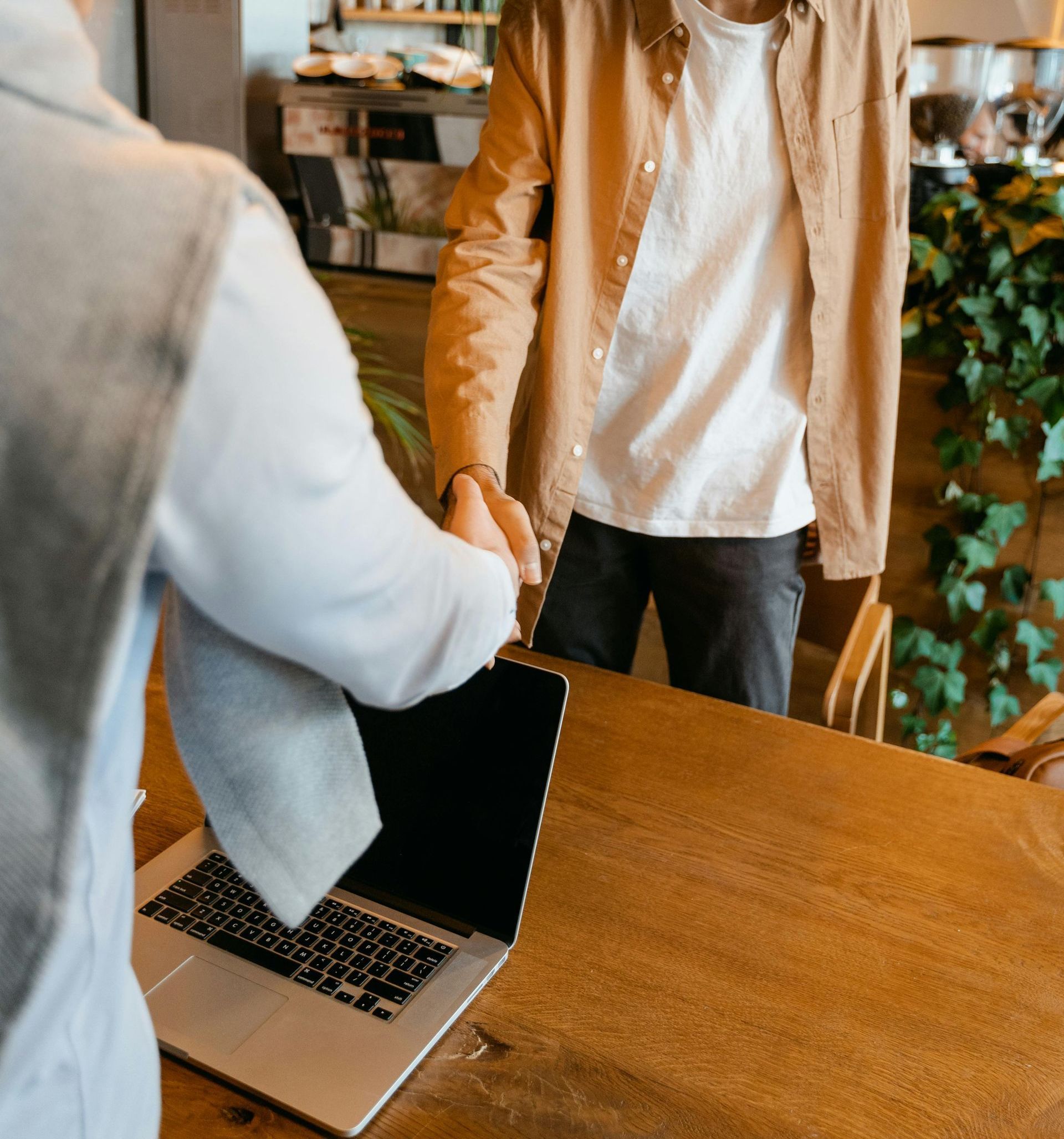 A man shaking hands with another man in front of a laptop
