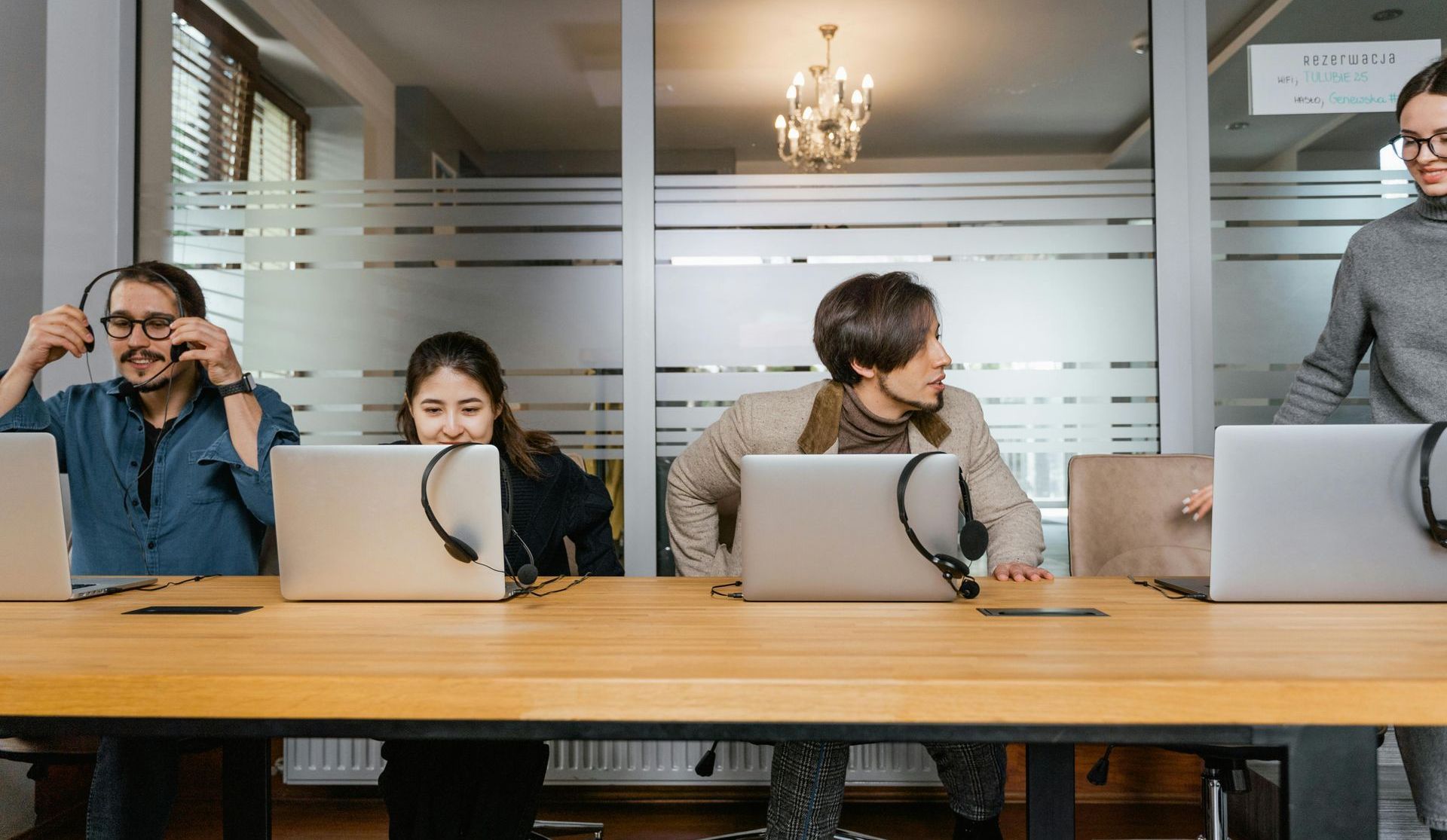 A group of people are sitting at a table with laptops and headsets.