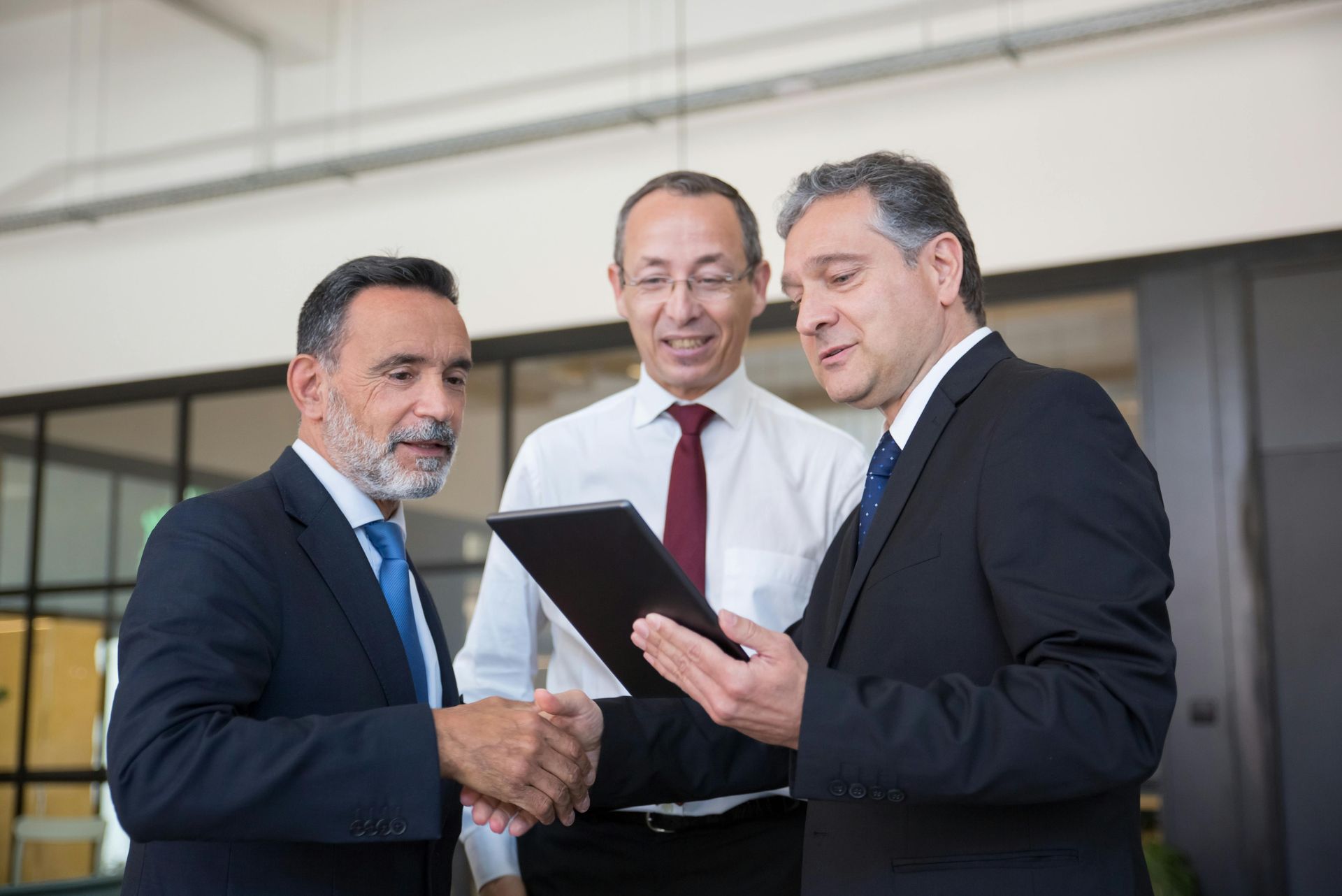 Three businessmen are shaking hands and looking at a tablet.