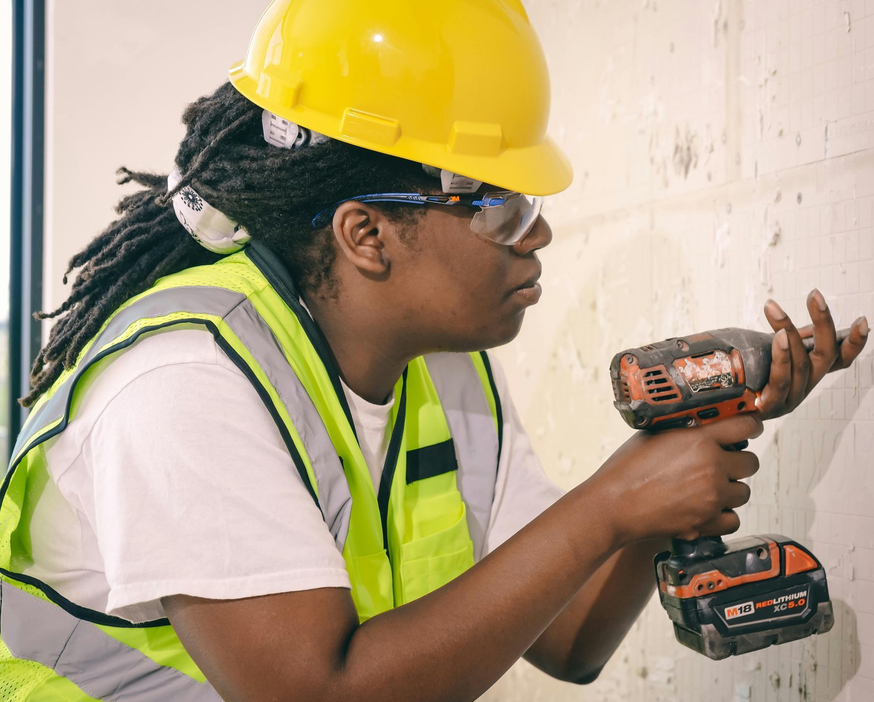 A woman wearing a hard hat and safety vest is using a drill.
