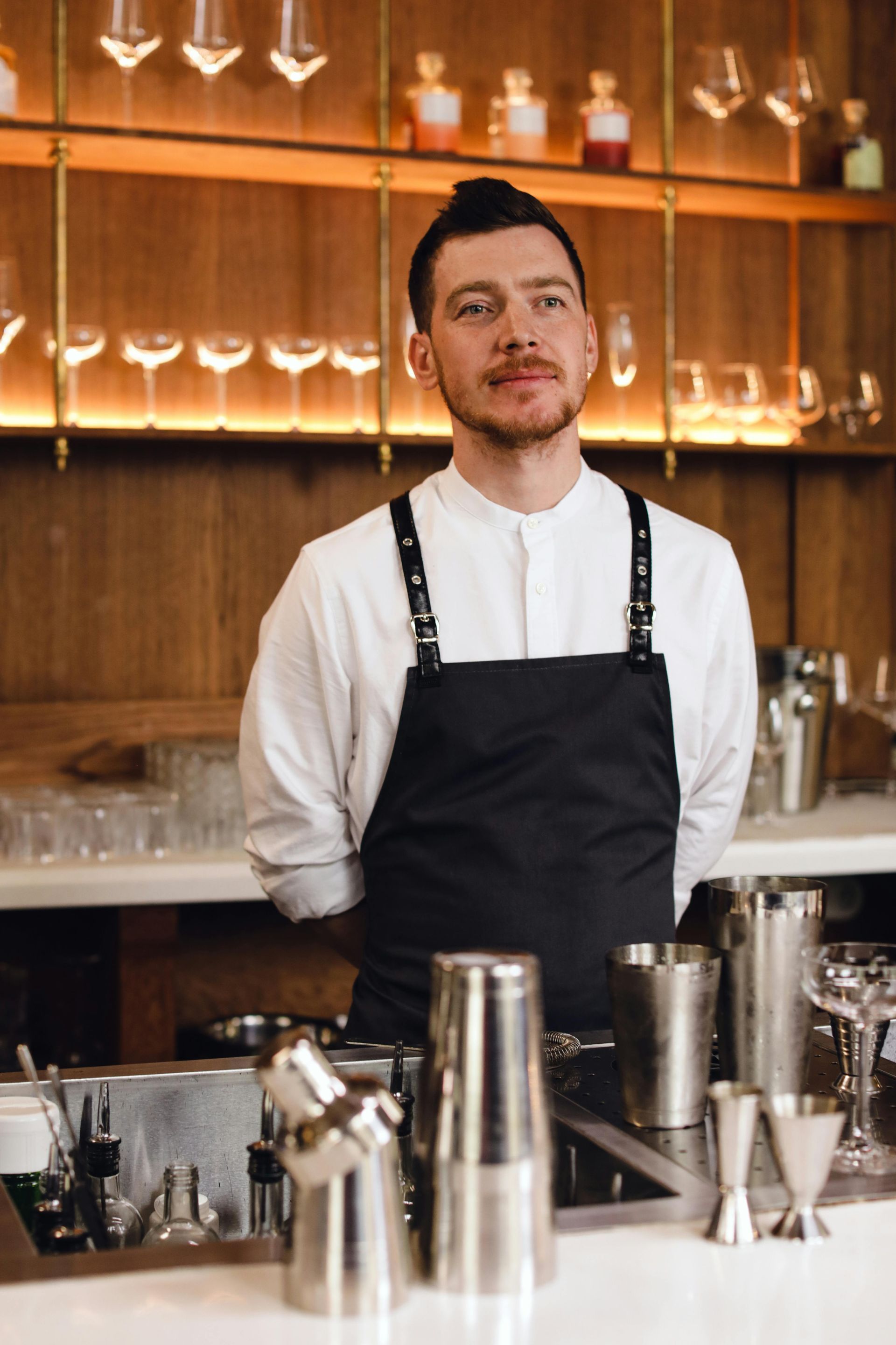 A man in an apron is standing behind a bar.