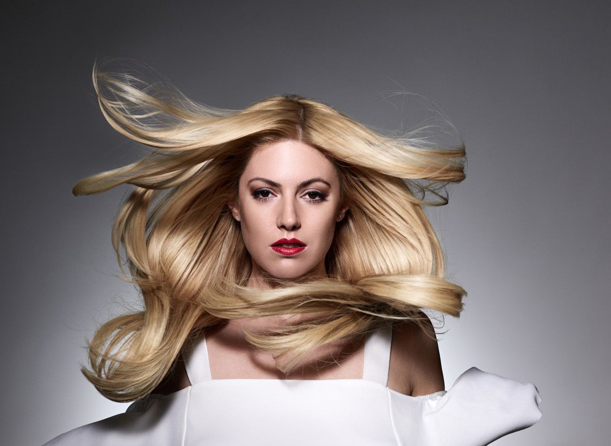 Blonde model with flowing hair and red lipstick against a gray background