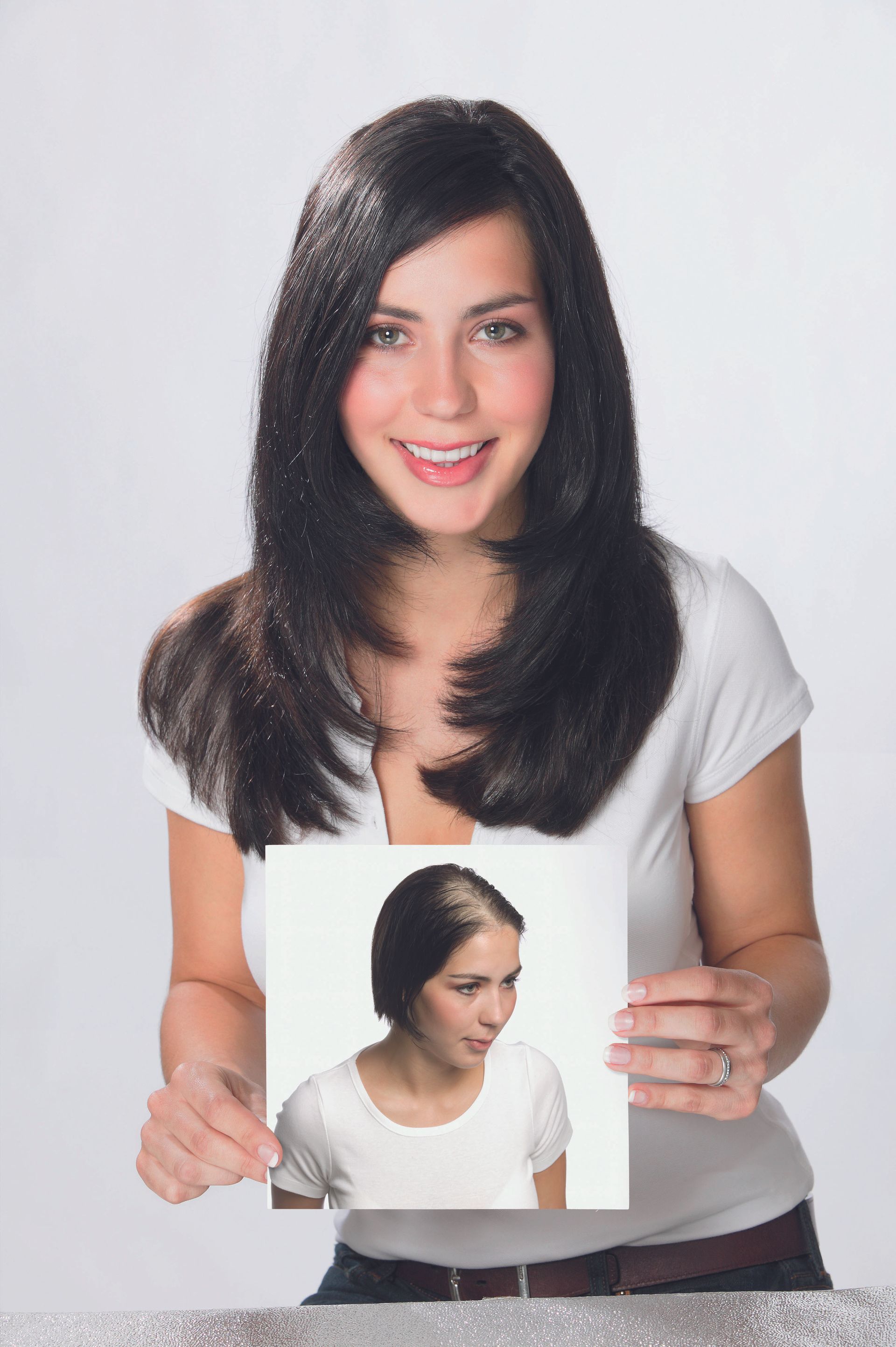 Woman in a white shirt holding a photo of a shorter hairstyle version of herself against a light background